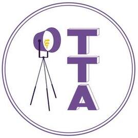 TTA Logo. A purple circle with the letters TTA displayed vertically and a purple light stands to the left of the letters
